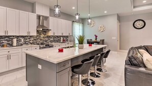 Una cocina moderna con armarios blancos, una isla central con taburetes de bar, iluminación colgante y salpicadero con baldosas blanco y negro.