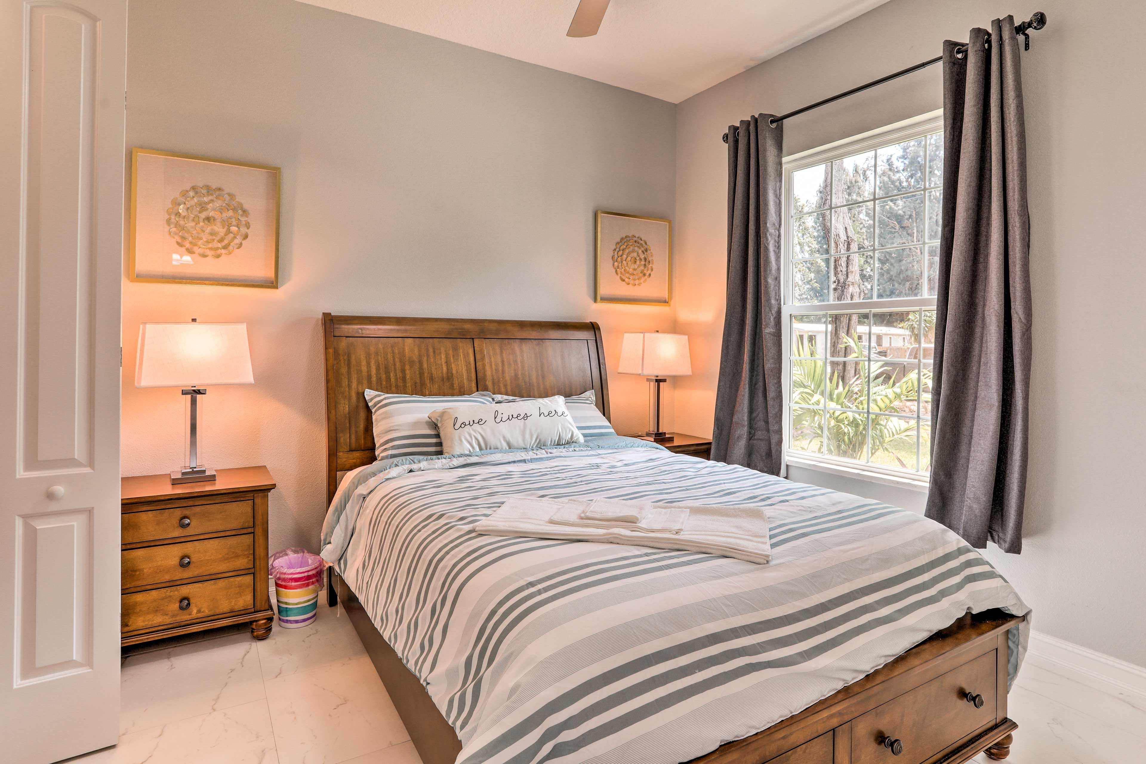 A neatly made bed with striped bedding, two bedside lamps, a wooden nightstand, and a window with curtains.
