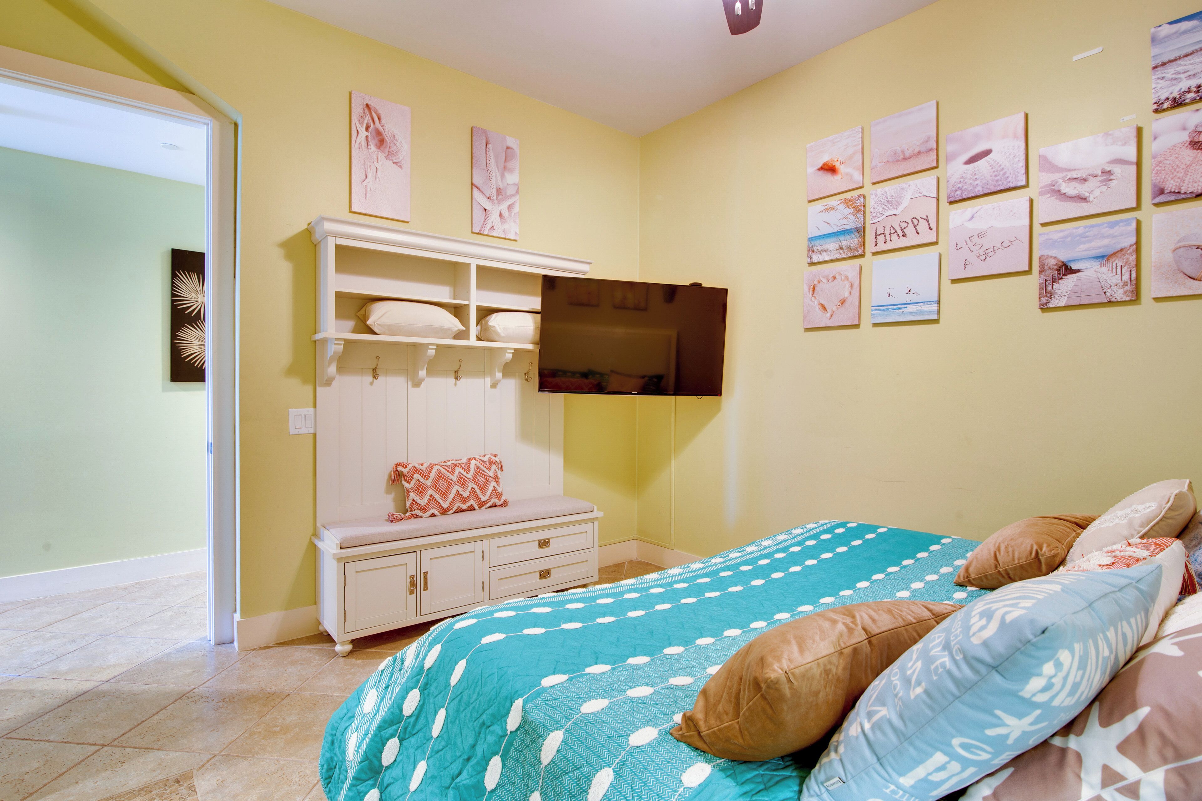 A bedroom with a bed, a white wardrobe, and a wall with framed pictures.