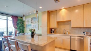 Uma cozinha moderna com ilha central, armários de madeira, eletrodomésticos de aço inoxidável e uma área de refeições com cadeiras e mesa.