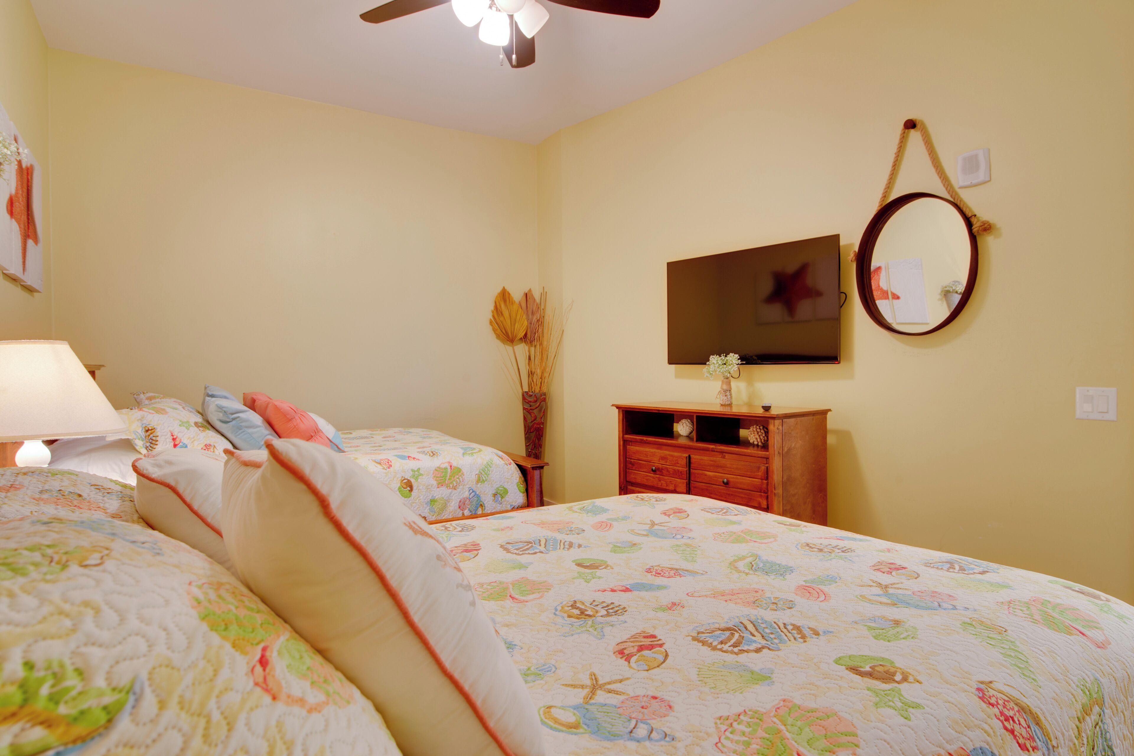 A bedroom with two beds, a dresser, a mirror, and a ceiling fan.