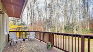 Une terrasse en bois avec deux fauteuils Adirondack, une plante en pot et une vue sur une forêt aux couleurs automnales.
