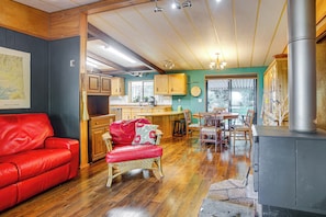 A cozy living room with a red sofa, wicker chair, wooden cabinets, and a large window. - Secluded Port Townsend Retreat: Pets Welcome! (Port Townsend)