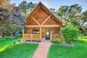 Cozy cabin-style building with a gabled roof and inviting front porch, set amidst a beautifully manicured lawn and lush surroundings.