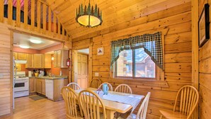 A wooden cabin interior with a dining area, kitchen, and a window with a checkered curtain. - Pet-friendly Warrens Cabin w/ Fire Pit! (Warrens)