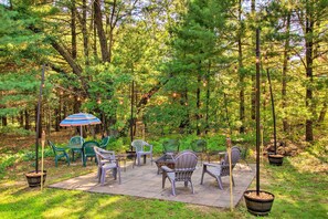 Relax in a serene outdoor setting surrounded by lush greenery and tall trees, with comfortable seating and tables on a paved patio.