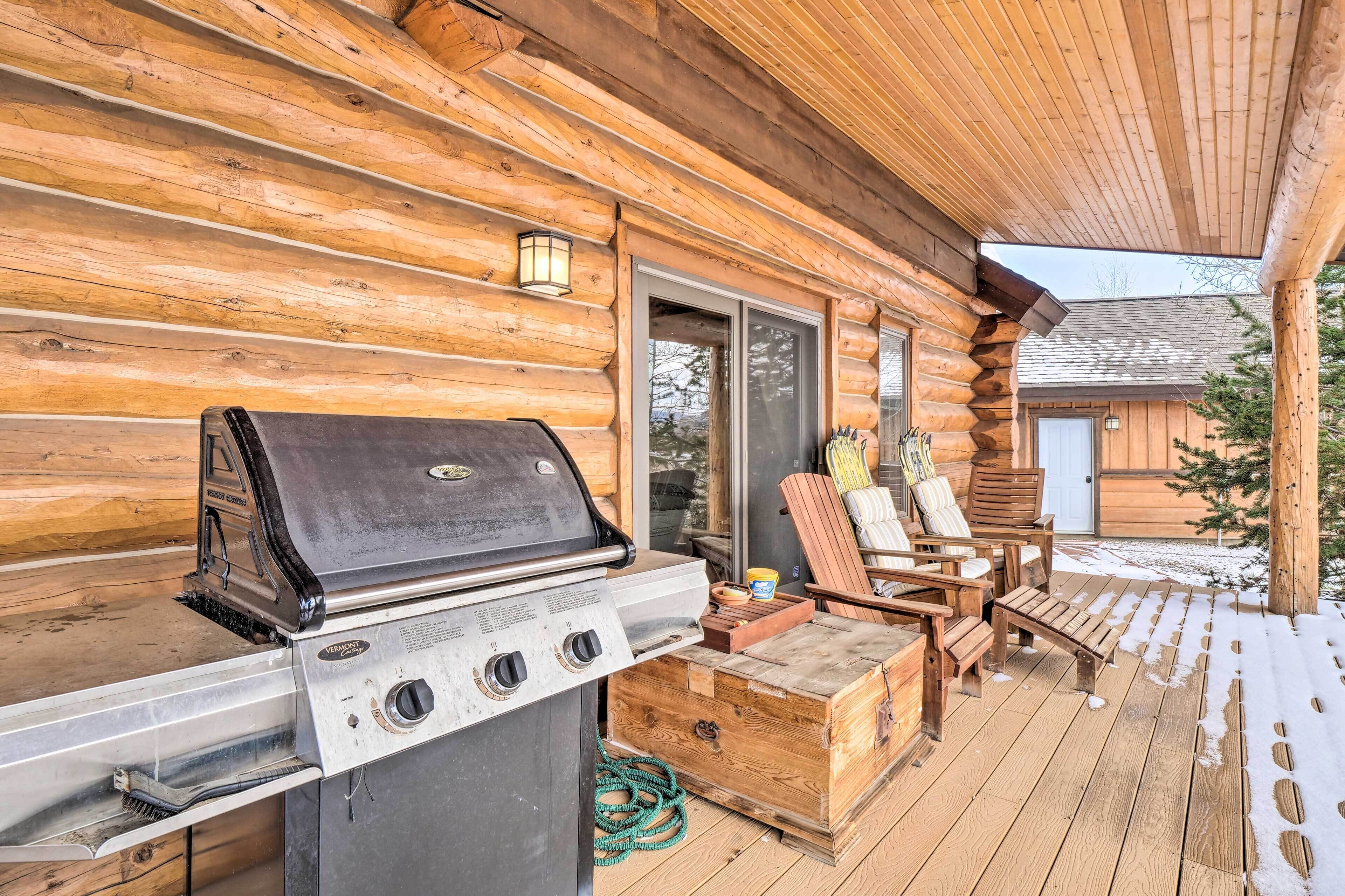 A wooden deck with a grill, outdoor seating, and a view of a cabin.