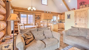 A cozy log cabin interior with a large sofa, wooden dining table, and a kitchen area. - Mountain Views & Fire Pit: Granby Retreat! (Granby)