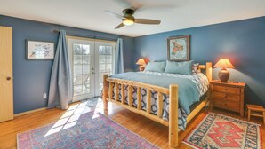 Ein Schlafzimmer mit einem hölzernen Bett, einem Deckenventilator, einem Nachttisch mit Lampe, einem Teppich und einer Tür, die auf einen Balkon führt.