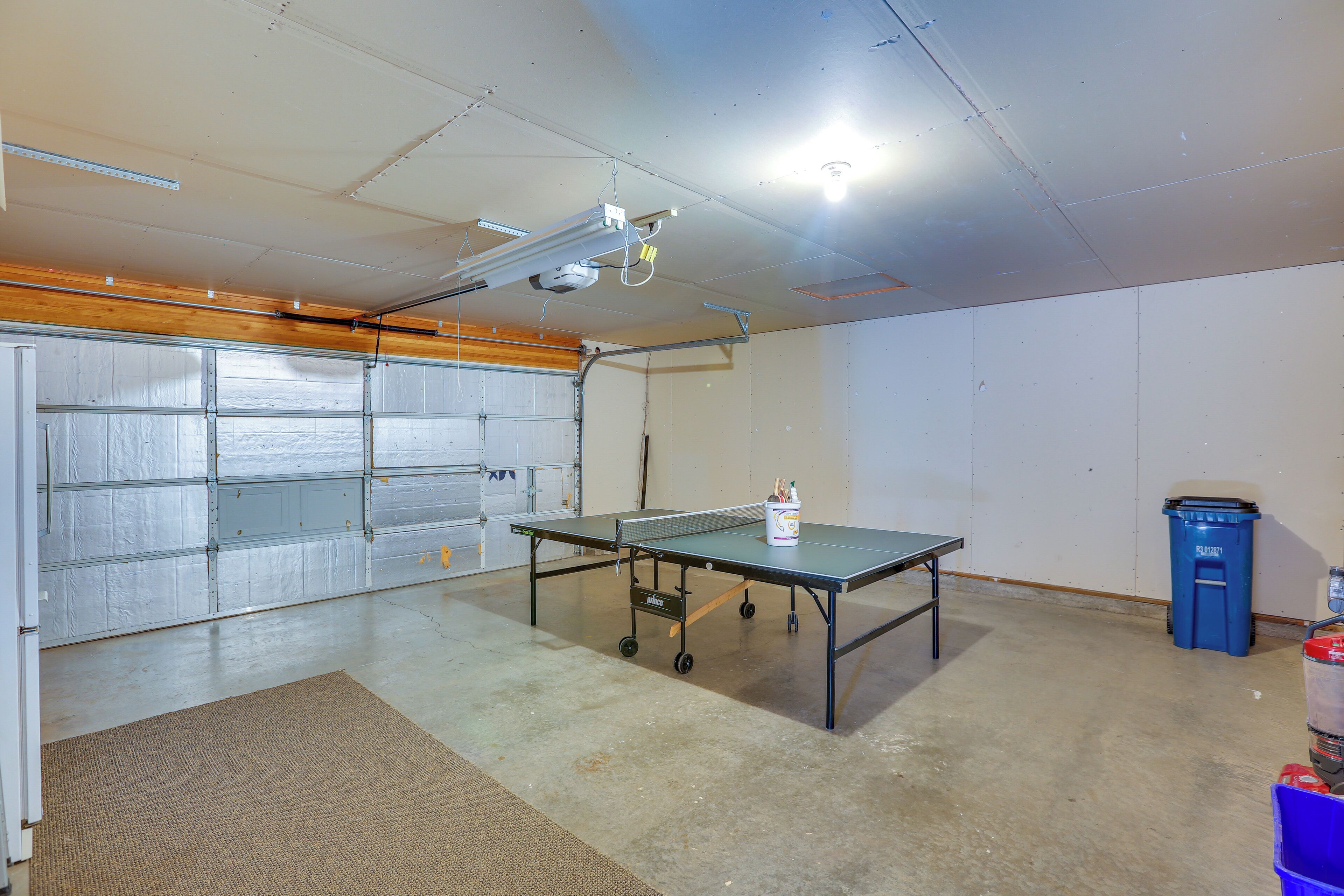A garage with a ping pong table, a projector, and a trash bin.