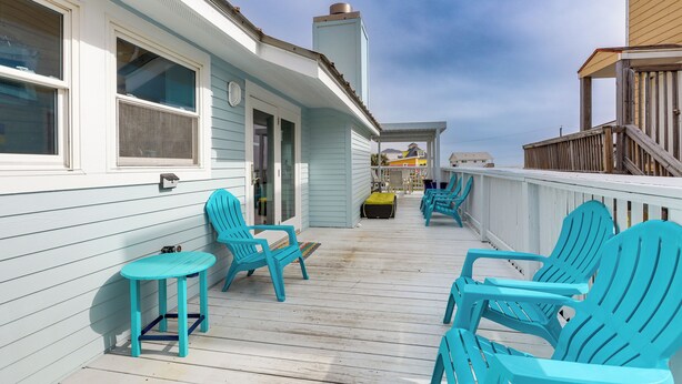 A wooden deck with turquoise Adirondack chairs and a small table, overlooking a beach. - Steps to Beach: Galveston Vacation Rental! (Galveston)