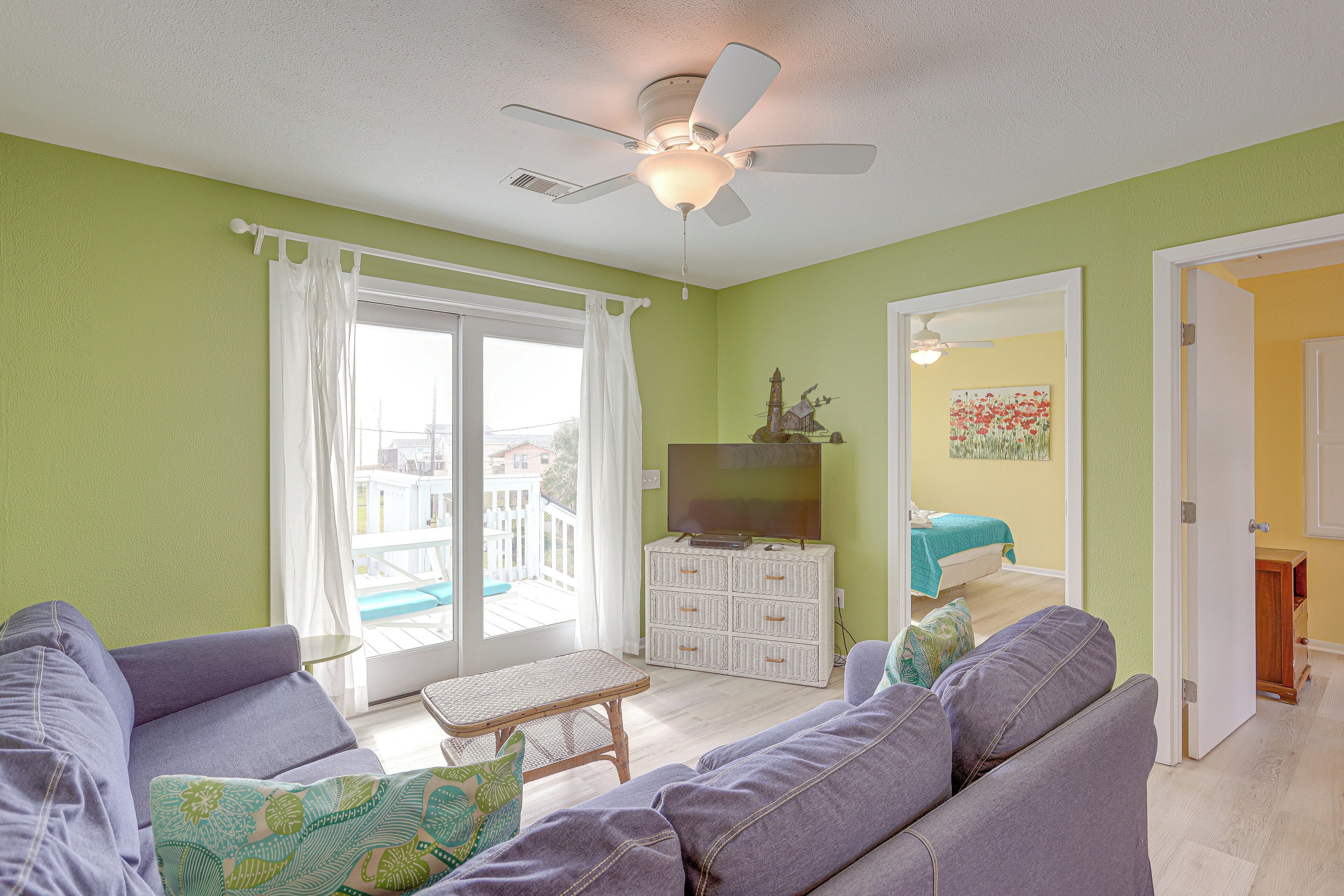 A living room with a sofa, a small table, a ceiling fan, and a television on a white dresser.