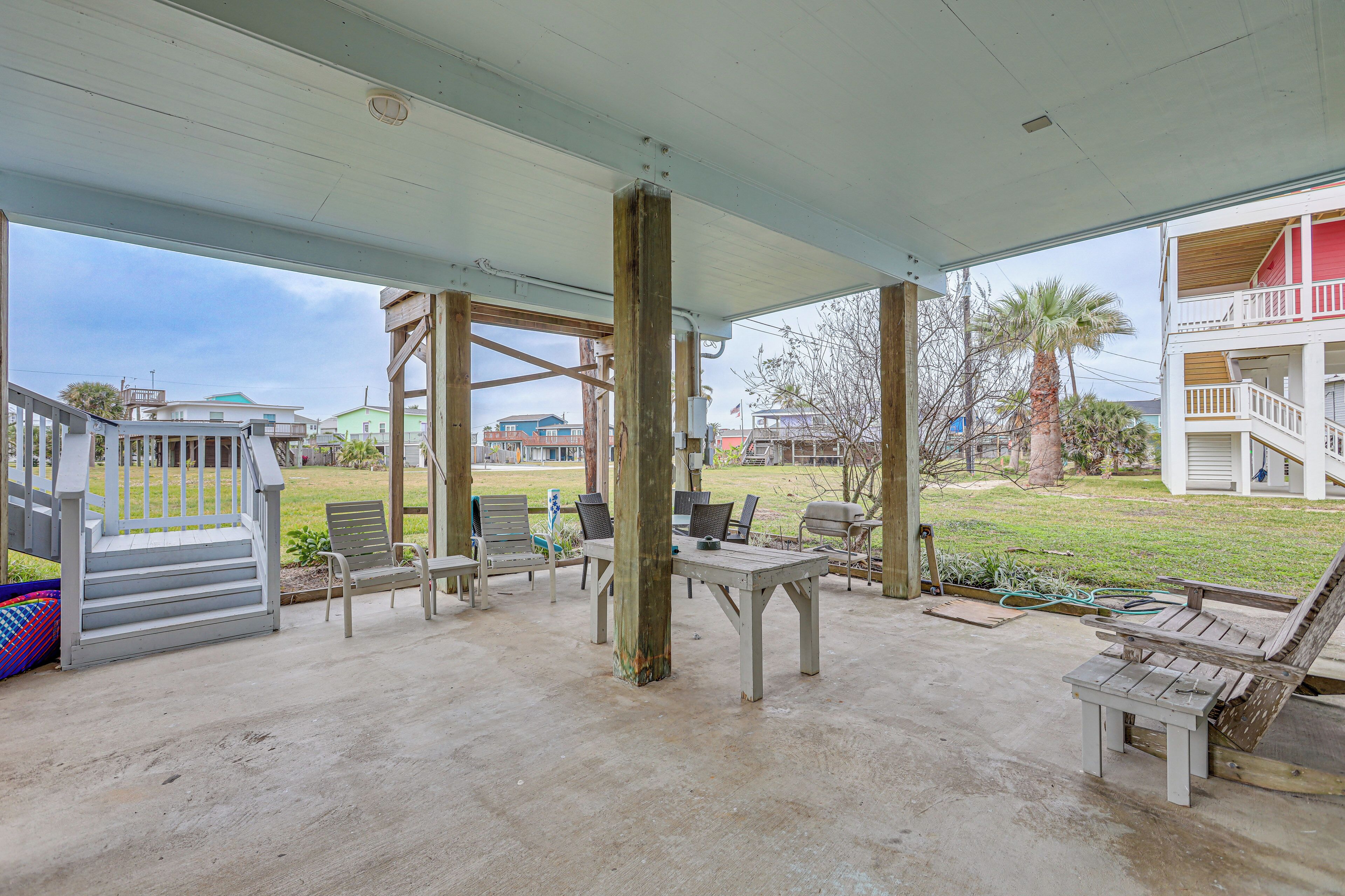 A covered outdoor patio with a concrete floor, wooden furniture, and a view of the surrounding neighborhood.