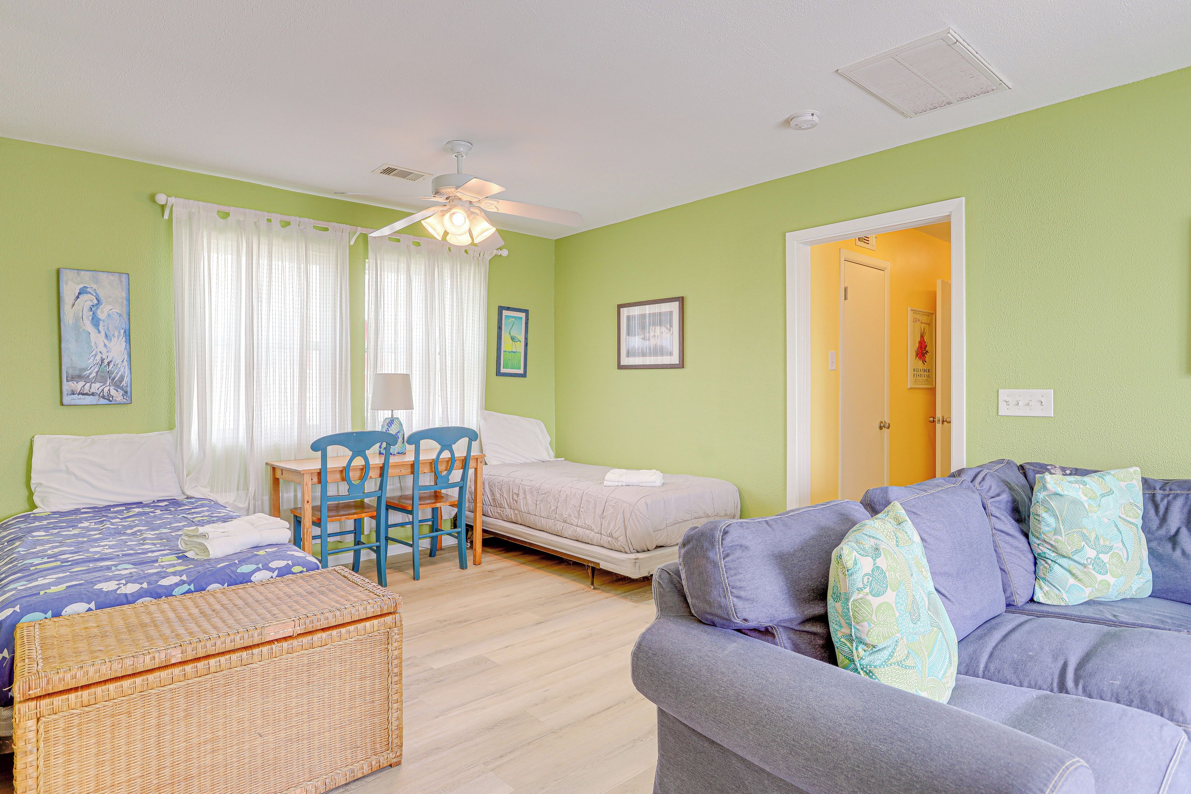 A room with a bed, a sofa, a chair, a table, and a ceiling fan.