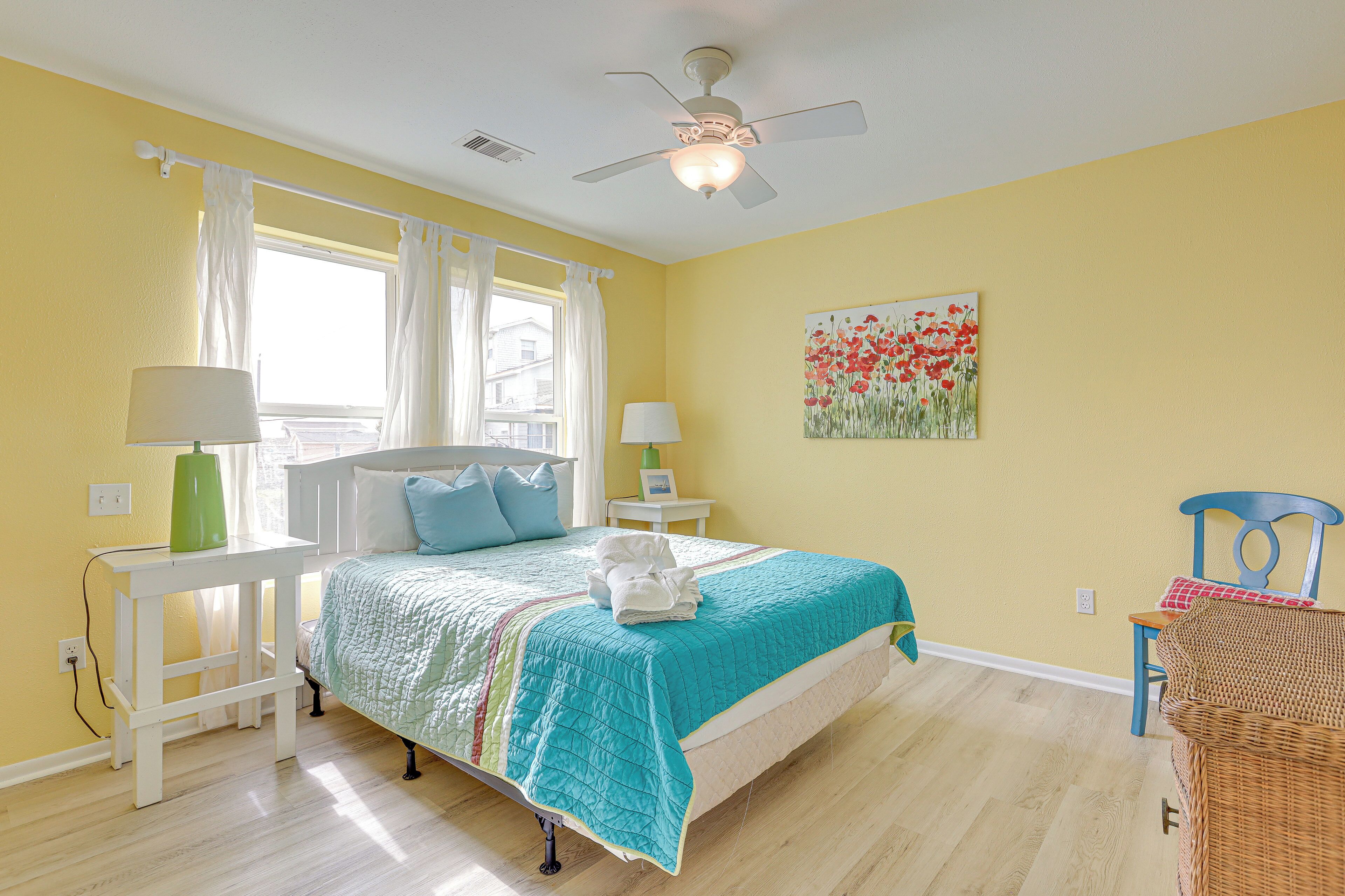 A bedroom with a bed, two bedside tables, a chair, a ceiling fan, and a window with curtains.