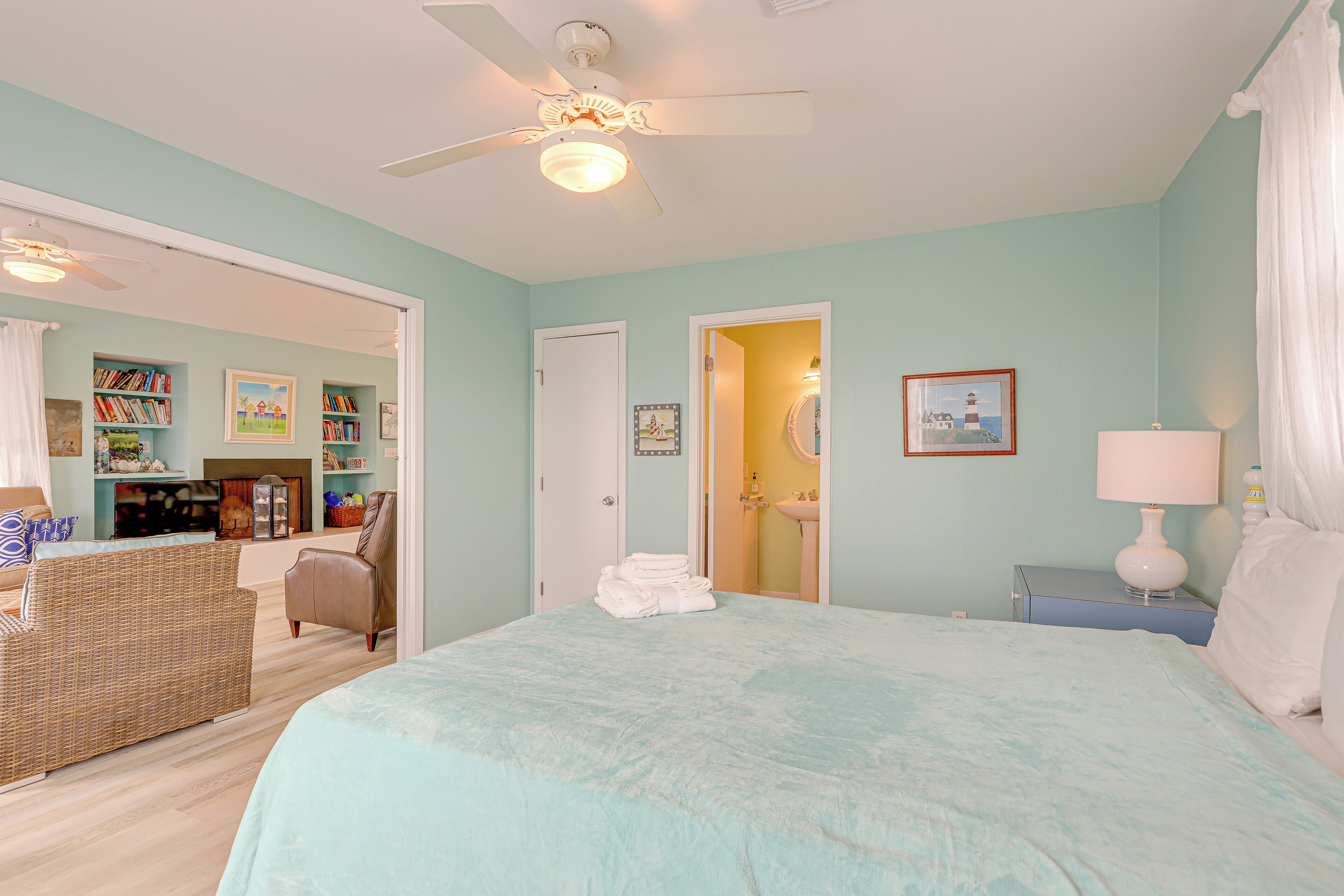 A bedroom with a large bed, a ceiling fan, a bookshelf, and a bathroom visible through an open door.