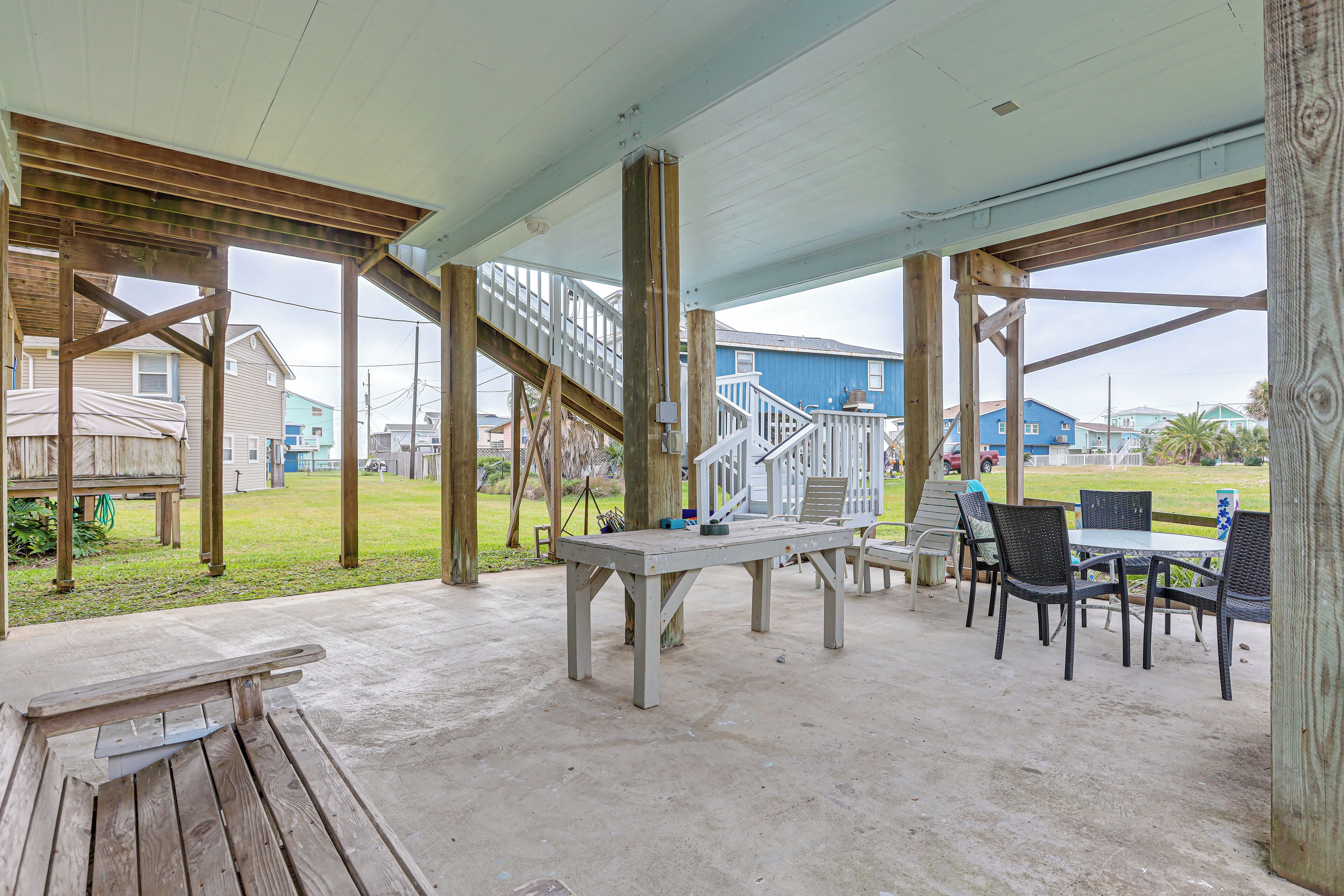Un espace extérieur abrité, doté d’un sol en béton, de tables et de chaises en bois, et d’un escalier menant à un niveau supérieur.