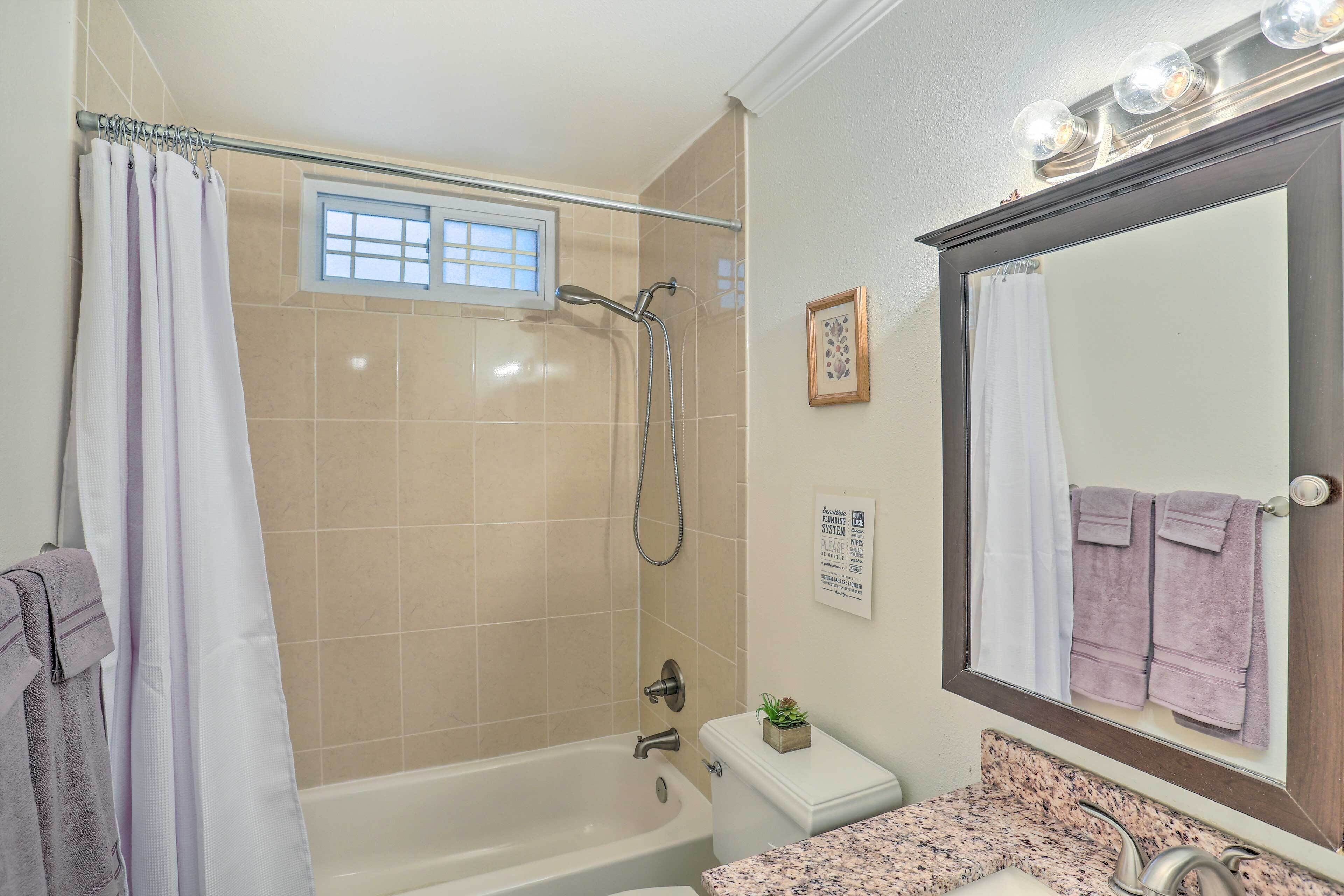 A bathroom with a bathtub, a shower, a sink with a mirror, and a window above the shower.