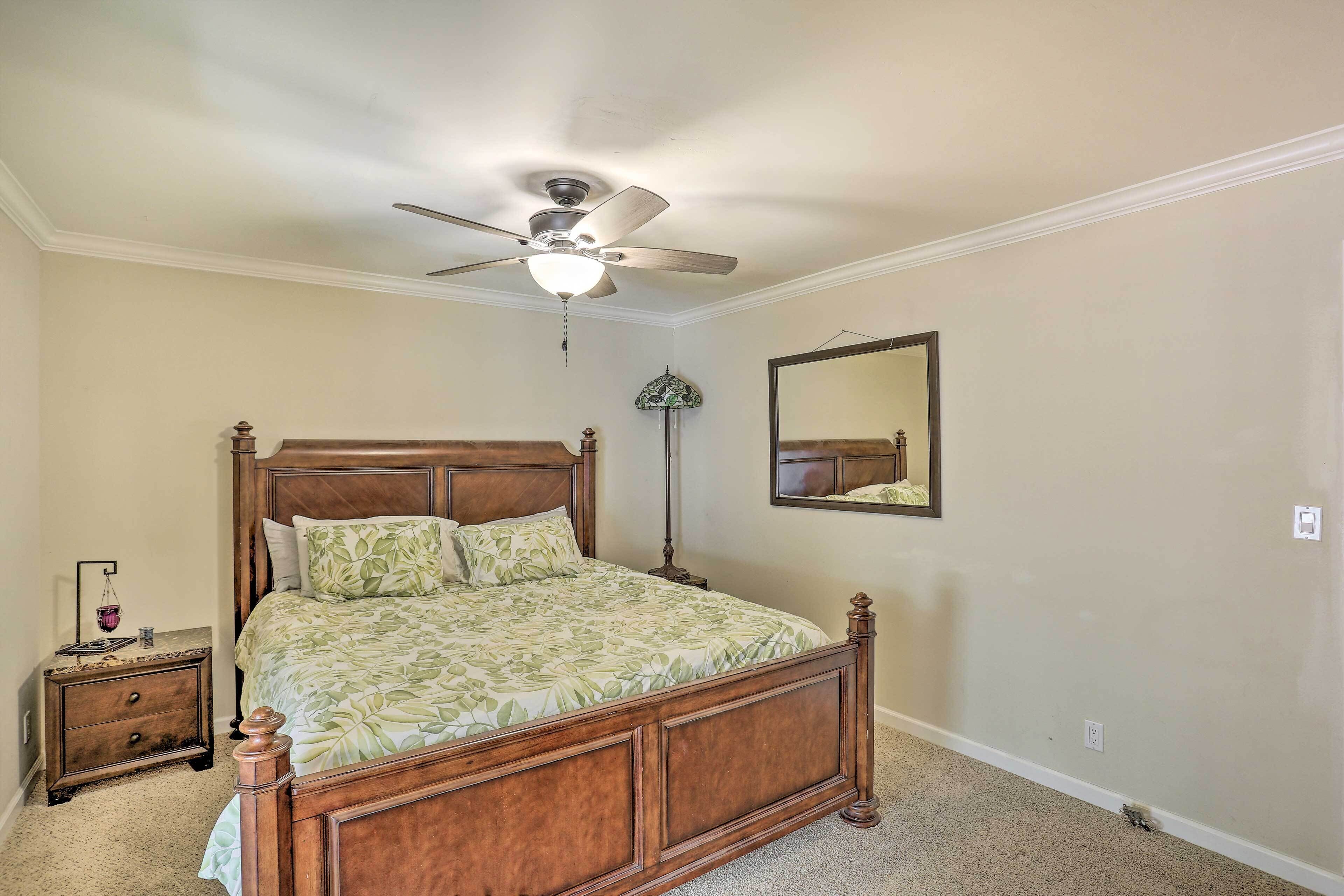 A bedroom with a wooden bed, a ceiling fan, a nightstand, a lamp, and a mirror on the wall.