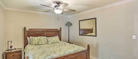 A bedroom with a wooden bed, a ceiling fan, a nightstand, a lamp, and a mirror on the wall.