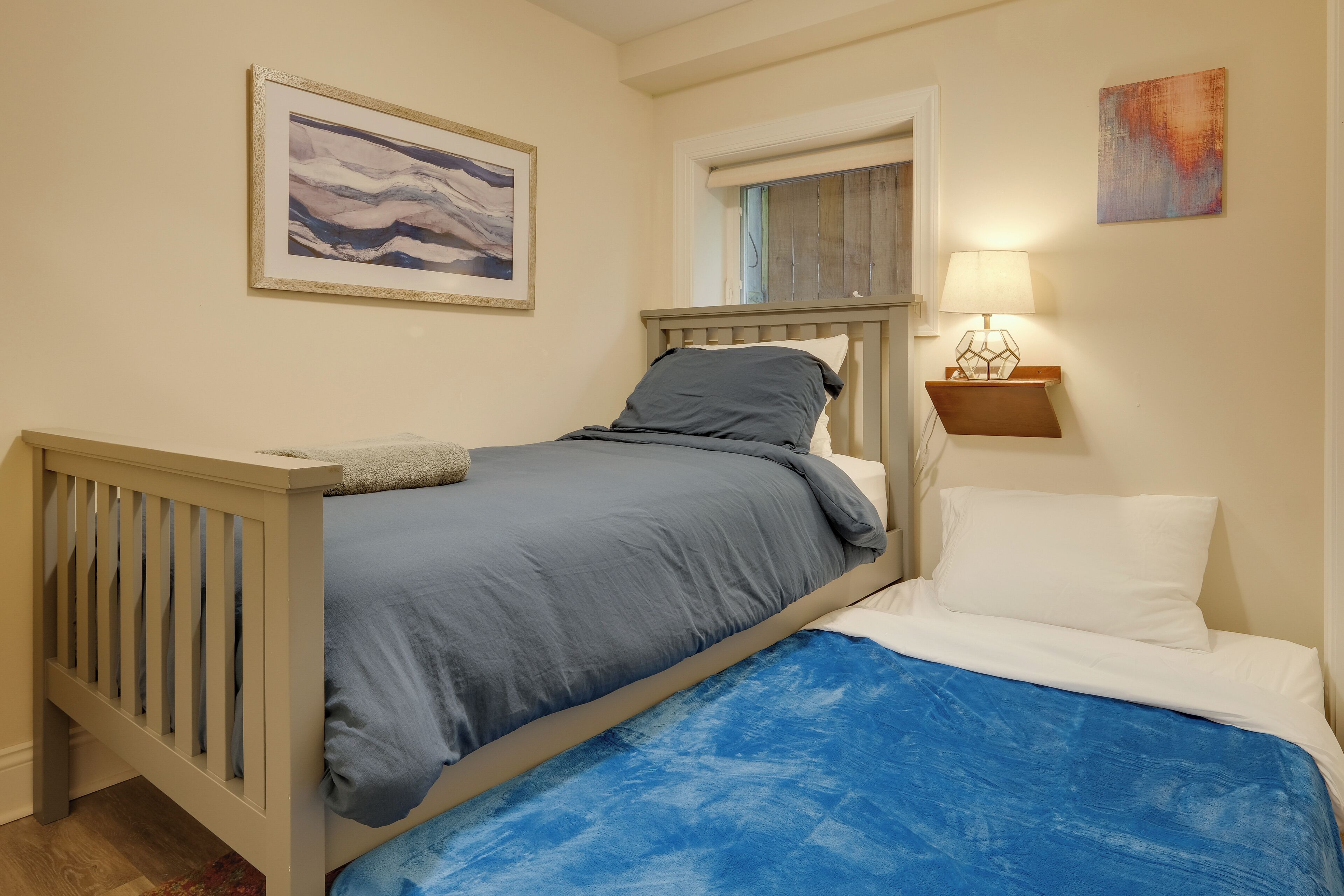 A bedroom with a bed, a nightstand, a lamp, and a painting on the wall.