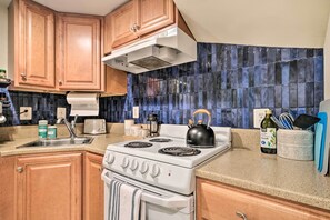 A kitchen with wooden cabinets, a white stove, a blue-tiled backsplash, and various kitchen items. - Washington DC Apartment at Rock Creek Park! (Washington)