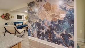 Ein Wohnzimmer mit blauem Sofa, Couchtisch und einer Wand mit einem Wandgemälde zum Thema Natur.