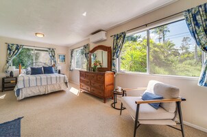 Un dormitorio con cama, cómoda, silla y ventanas grandes con cortinas.