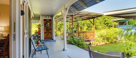 A covered porch with outdoor seating, a wooden door, and a view of a lush garden.