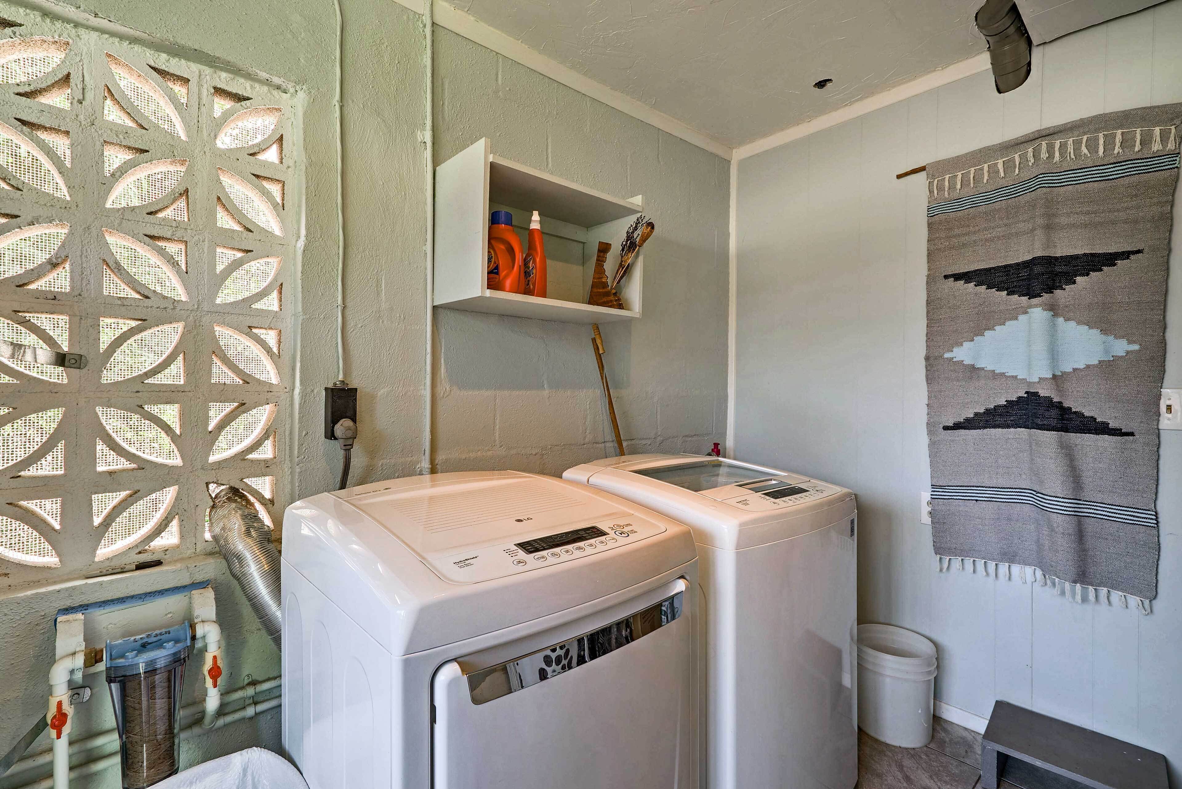 A laundry area with two washing machines, a shelf with cleaning supplies, a window with a decorative screen, and a wall-mounted towel.