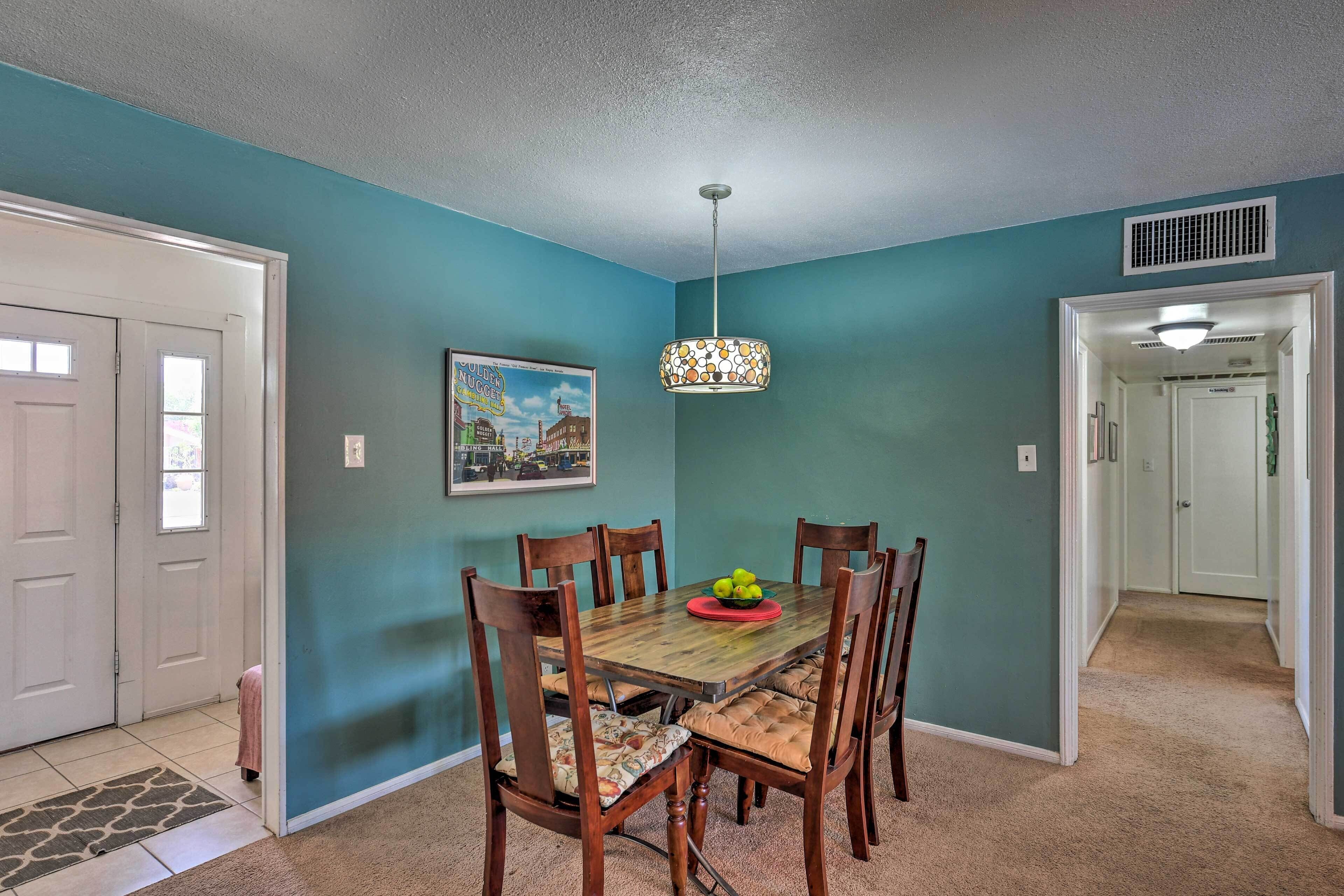 Un coin repas avec des murs de couleur turquoise, une table en bois et six chaises. Un luminaire suspendu se trouve au-dessus de la table.
