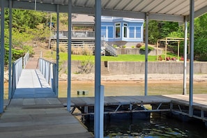 A covered dock leading to a house with a blue exterior, a grassy area, and a small bridge.