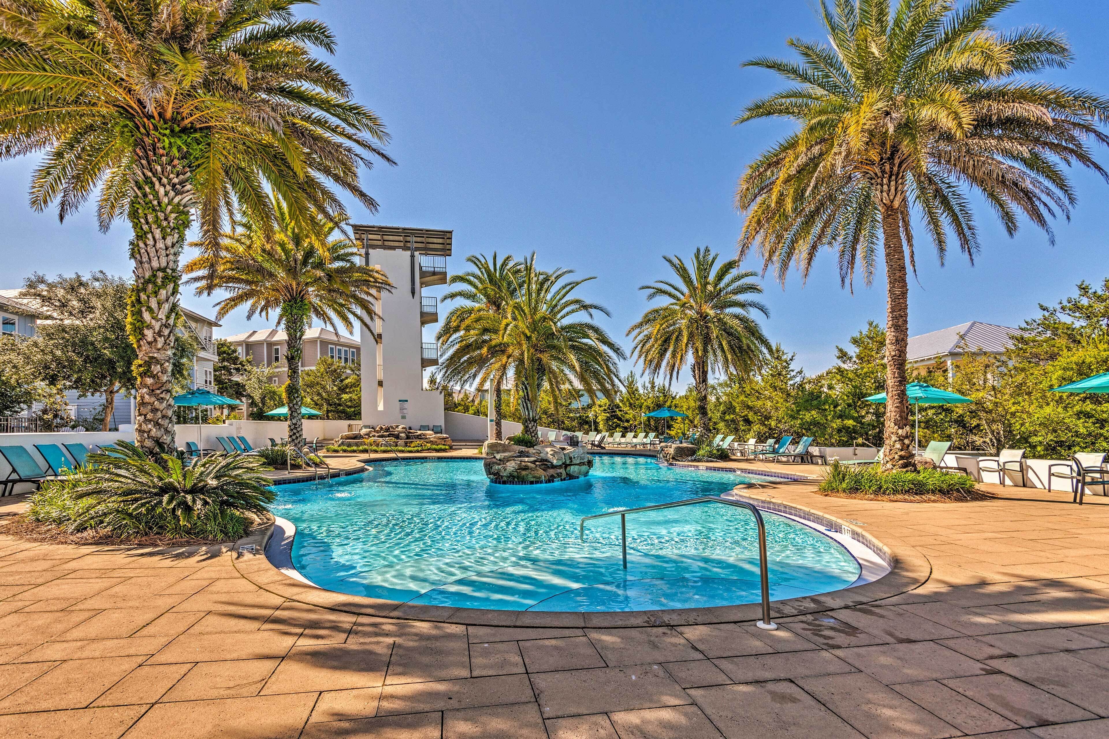 A pool area with palm trees, lounge chairs, and a clear blue sky.