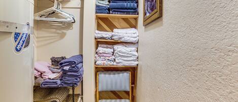 A laundry area with shelves of folded towels, a drying rack, and a wooden chair.