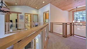 A spacious room with wooden ceiling beams, a balcony with a glass railing, and a large window offering a view of the outdoors. - Close to Slopes: Forest-view Gem in Lake Tahoe (South Lake Tahoe)