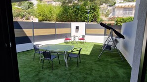 A balcony with a glass table, four chairs, a telescope, and a small table with a red cushion.