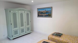 A room with a light green wardrobe, a framed painting of a coastal scene, and a floral-patterned bed.
