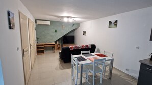 A compact living space with a dining area, a sofa, a TV, and a staircase.