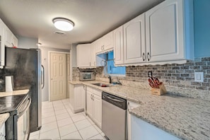 A kitchen with white cabinets, a granite countertop, a dishwasher, a microwave, and a knife block.