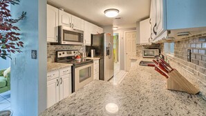 Una cocina con armarios blancos, electrodomésticos de acero inoxidable, encimeras de granito y un original bloc de cuchillos de madera.