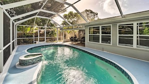 Una piscina con cerramiento de vidrio, rodeada por un patio con mobiliario exterior.