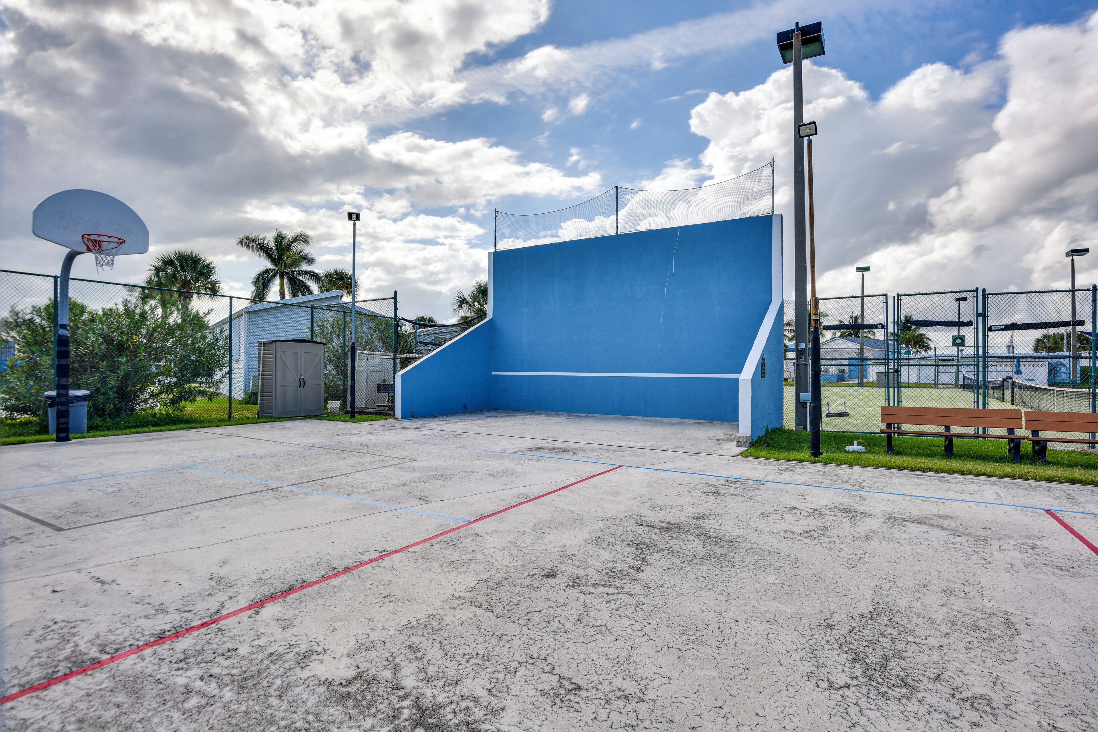 An outdoor basketball court with a blue wall, a basketball hoop, and a bench.
