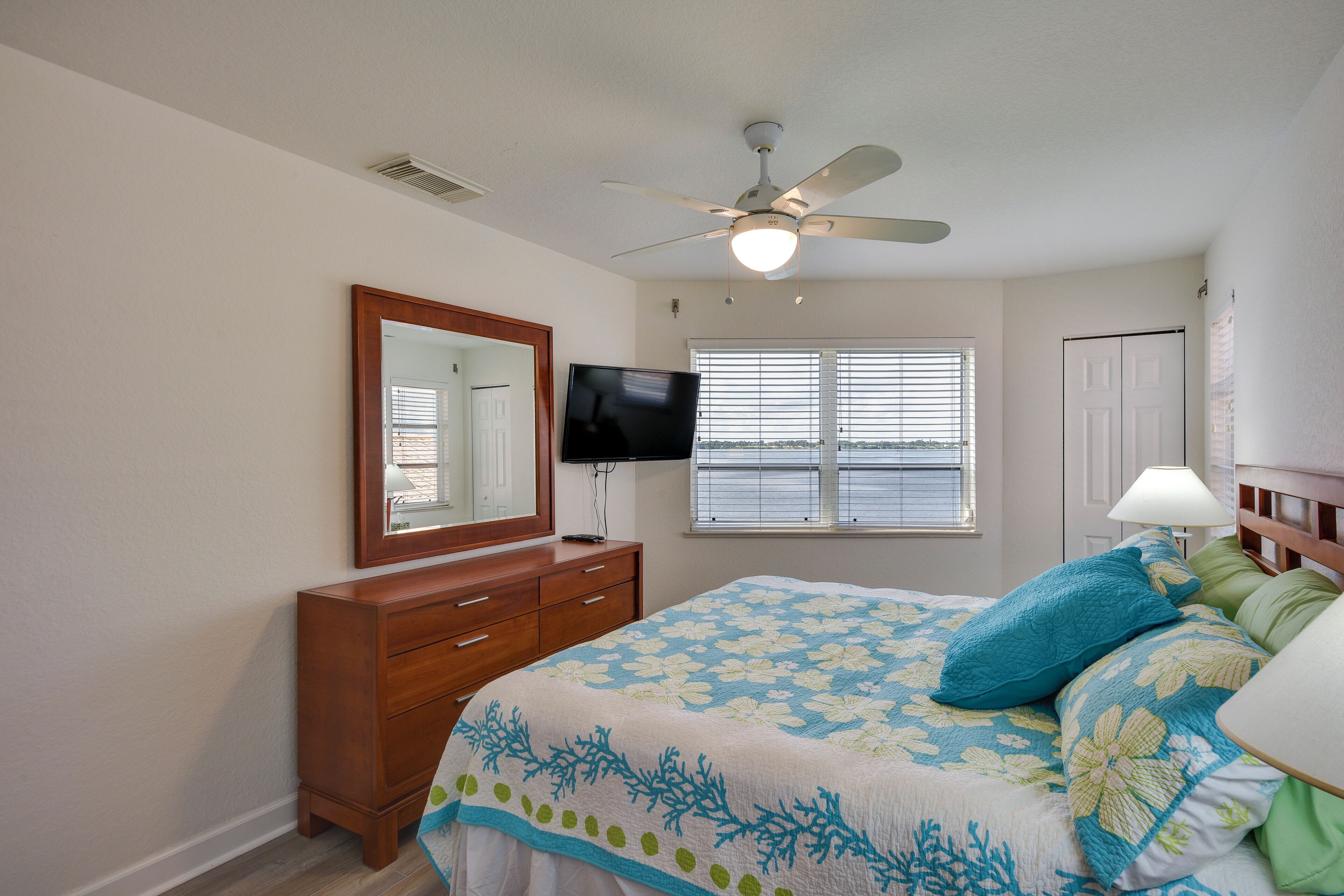 A bedroom with a bed, a dresser, a television, a ceiling fan, and a window with blinds.