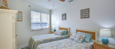 A bedroom with two beds, a ceiling fan, a window with blinds, and a nightstand with a lamp.