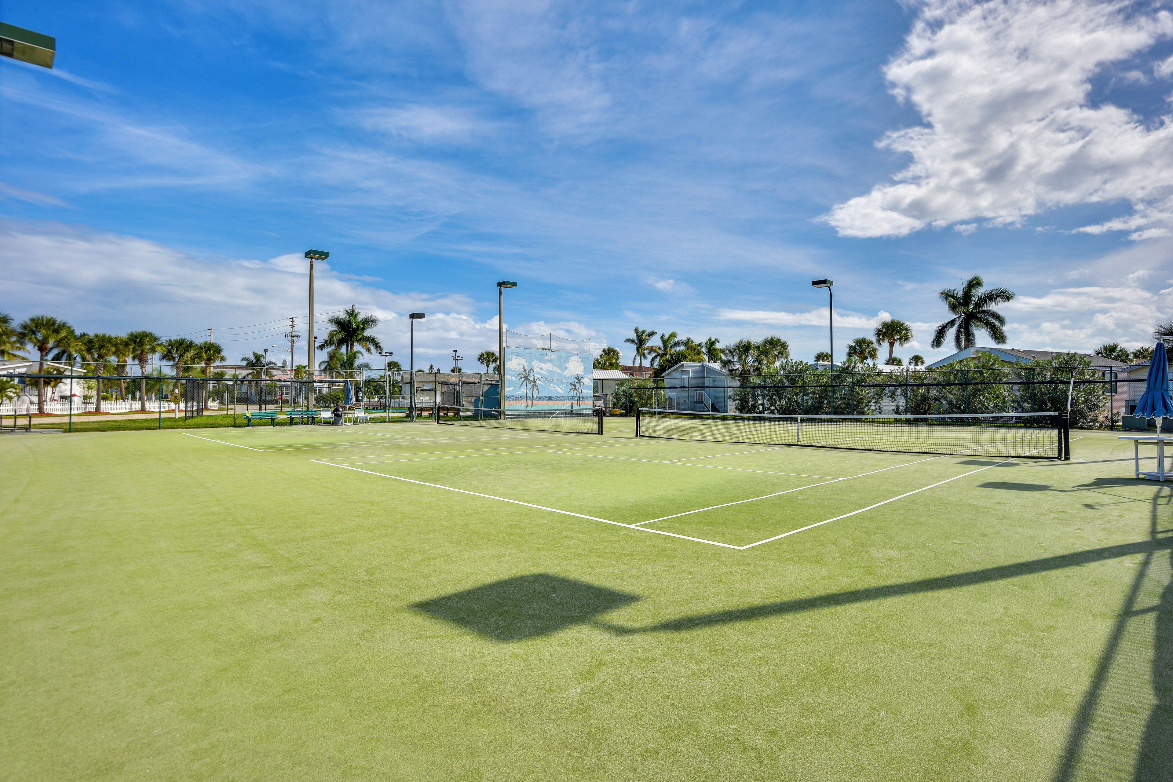 Ein Tennisplatz im Freien mit Netz, umgeben von Palmen und Gebäuden.