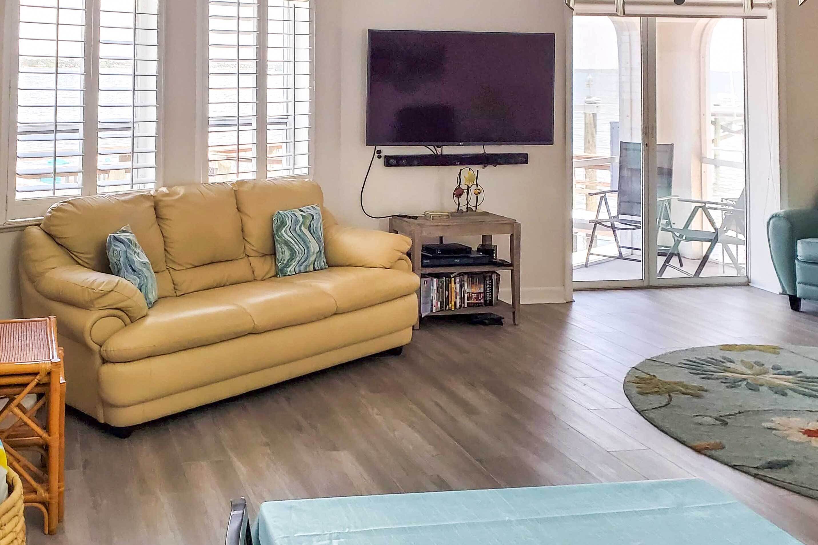 Un salon comprenant un canapé, un téléviseur à écran plat, une petite table avec des livres et une vue sur l’extérieur grâce à une porte vitrée.