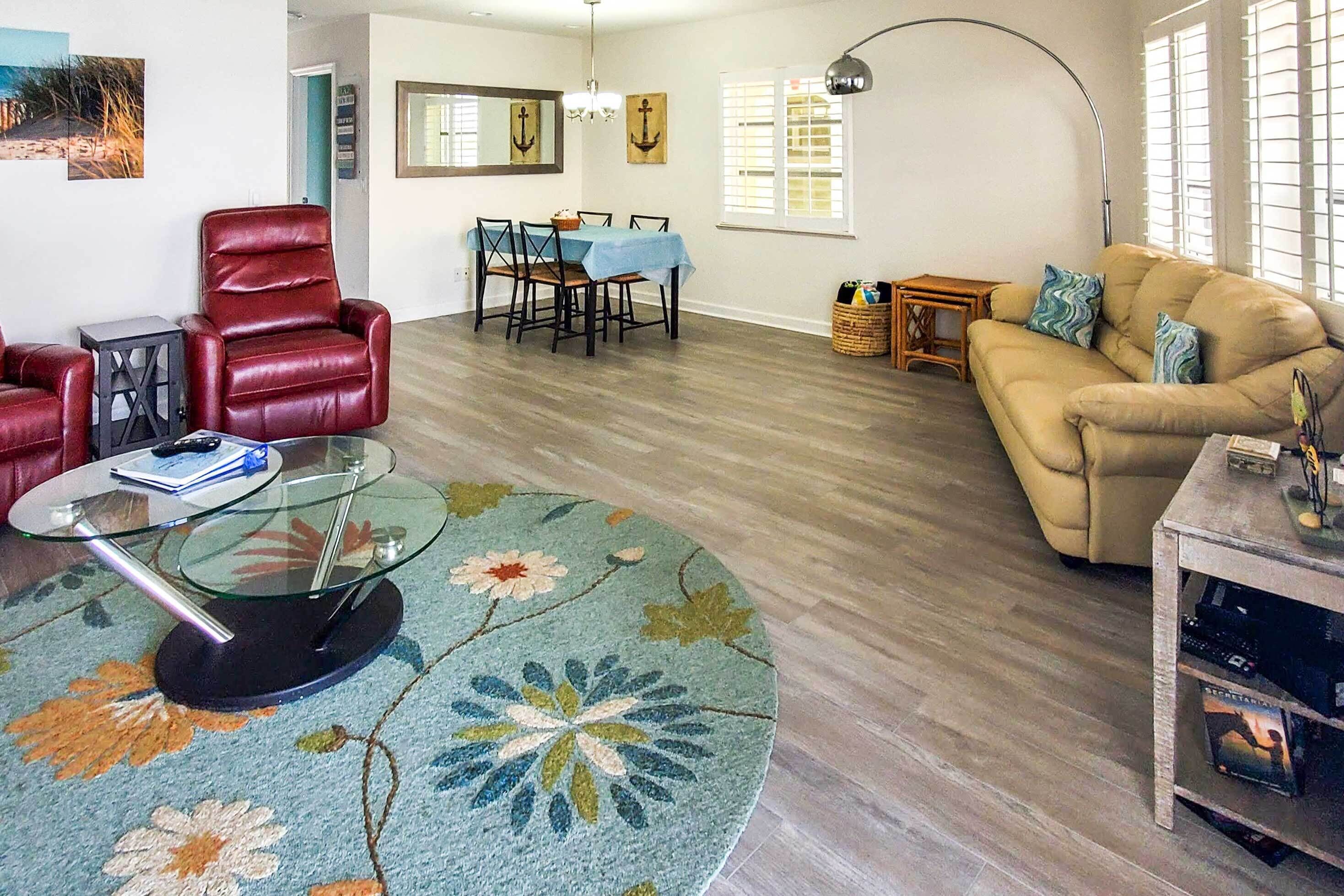 Una sala de estar con una mesa redonda, un sillón de cuero rojo, un sofá color beige y un comedor con mesa y sillas.