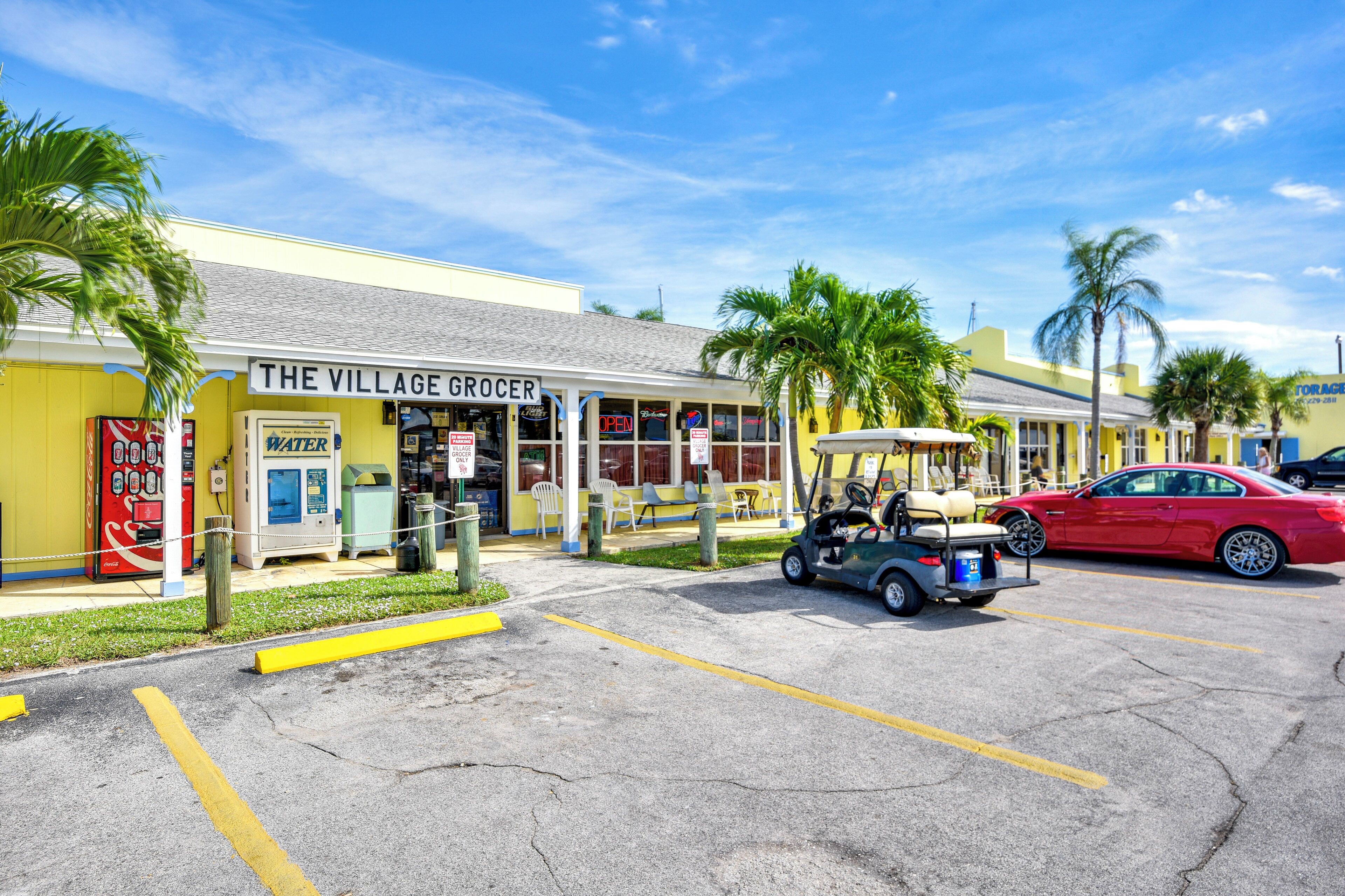 A yellow building with a sign reading "The Village Grocer" and a red car parked in front.