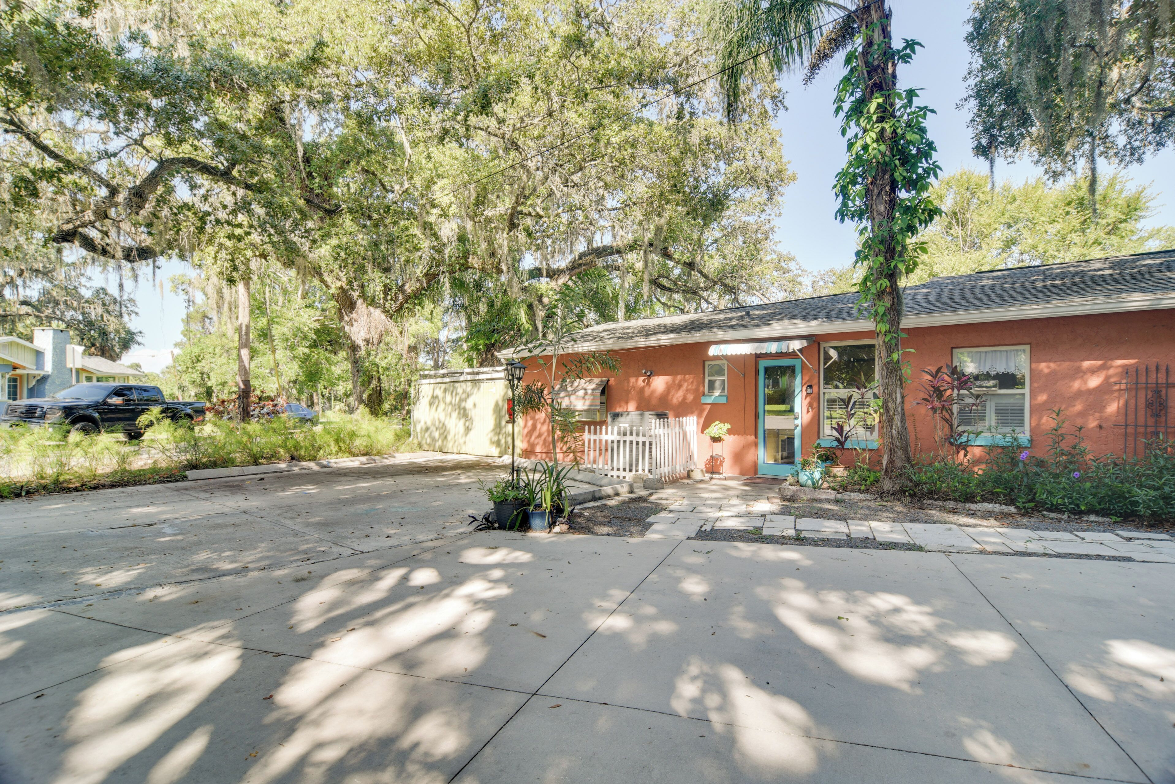 A single-story building with a red exterior, a front porch with a white picket fence, and a small garden area with potted plants.