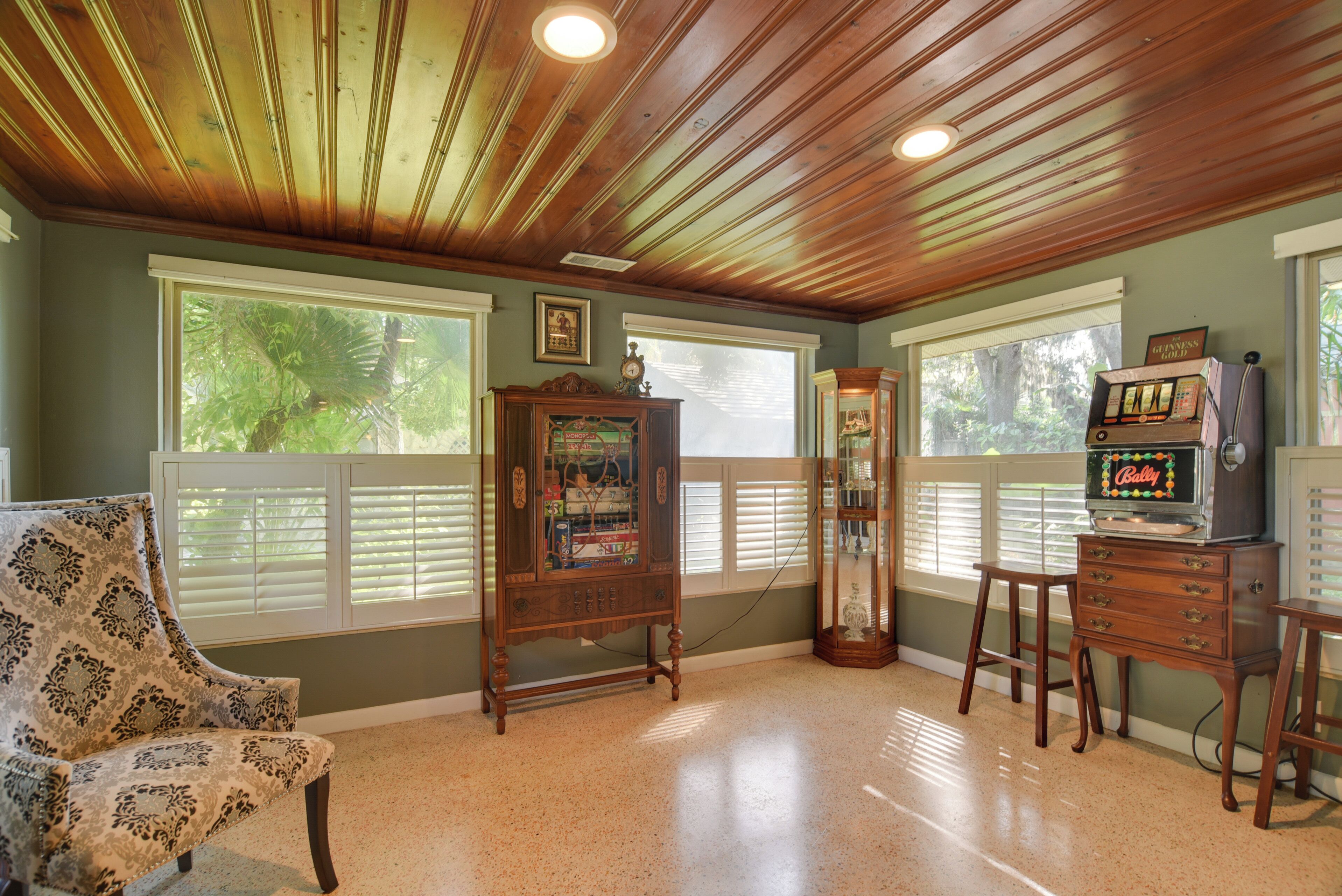 A room with wooden ceiling, a vintage radio, a television, and a patterned armchair.